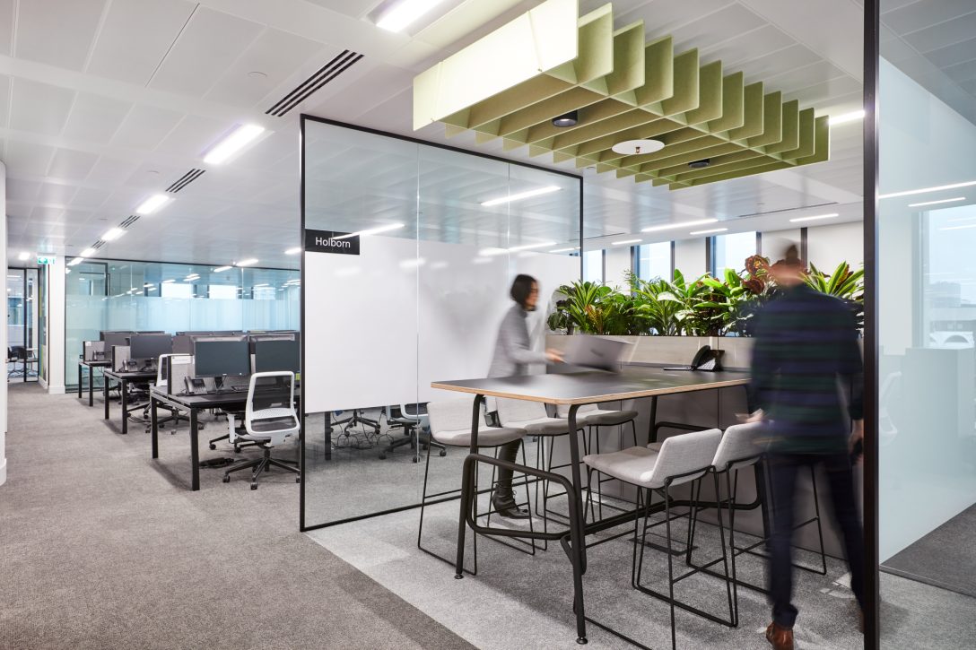 Two employees are shown about to sit down with a focus work area featuring acoustic baffles above head to enhance the overall office acoustics.