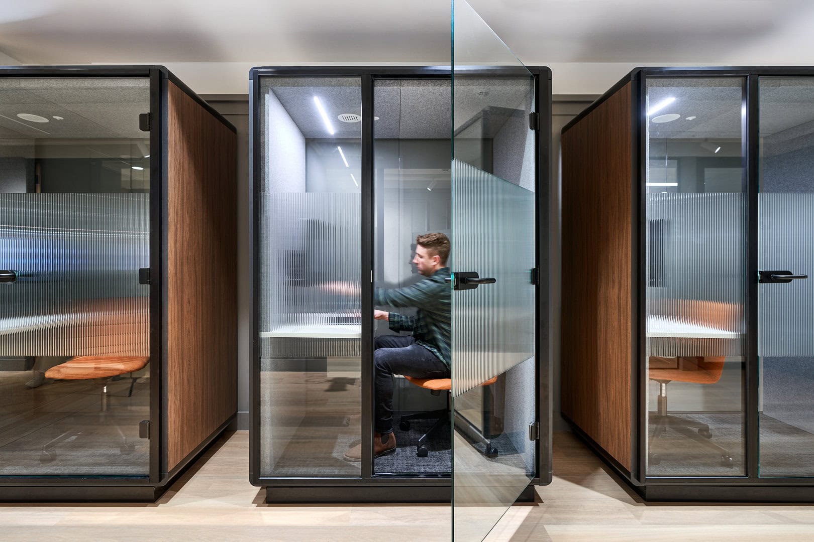 A man sits working in a privacy booth inside an office.