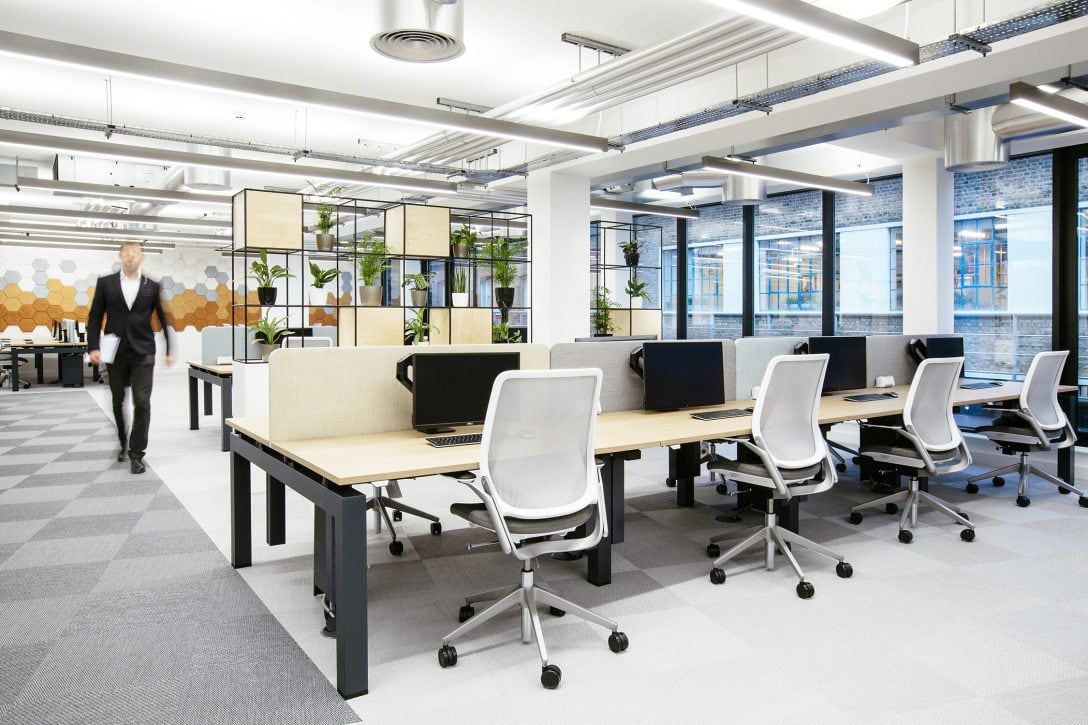 Inside an office where the main work zone is situated beside floor to ceiling windows allowing an abundance of natural light to flood the main productivity zone. 