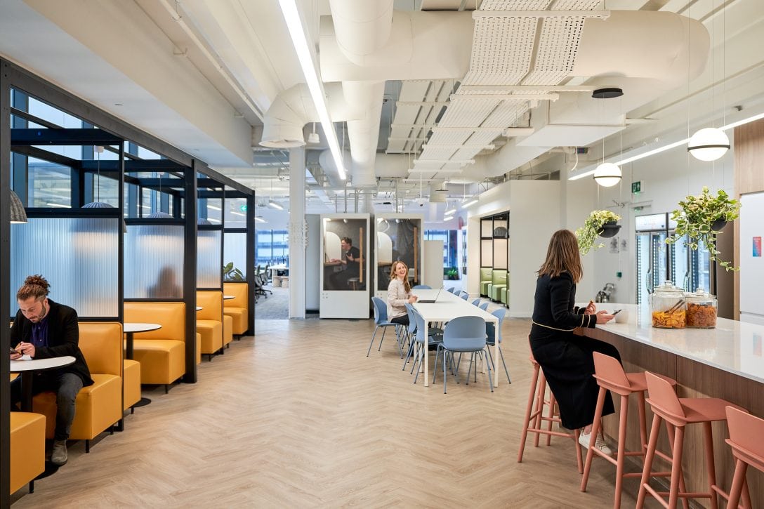 Employees are showing laughing together within the social space at Braze's office. The space features bench seating and collaborative booths. 
