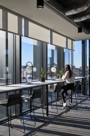 Employee sitting at high bench seating looking out onto city views.