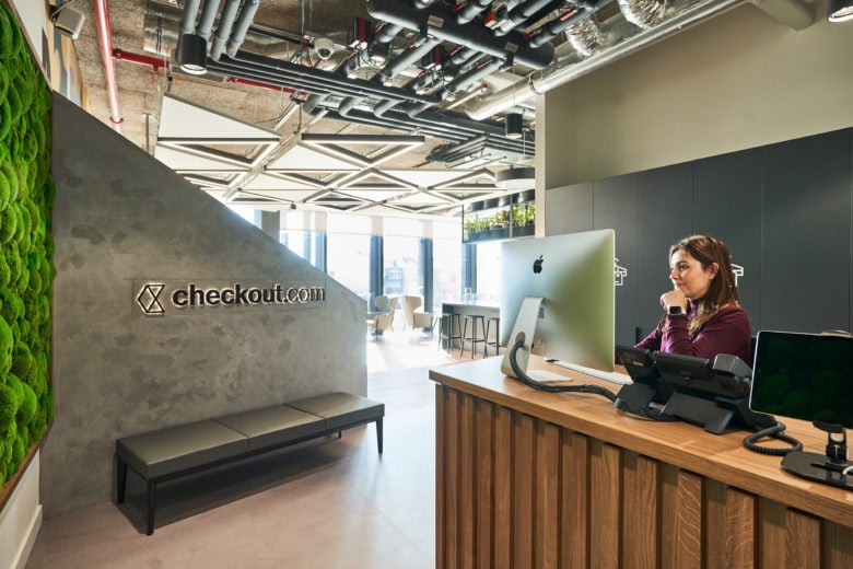 Workplace reception area with woman working behind desk and company graphic branding on wall.