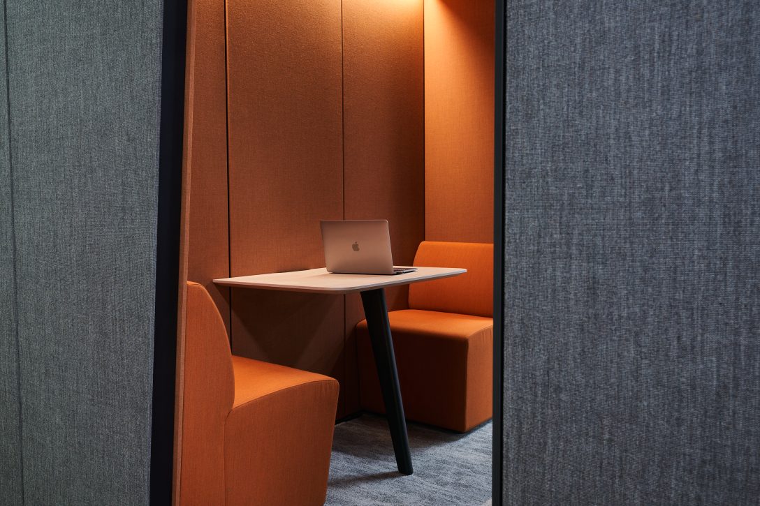 A laptop is sat open on the desk of a private work booth inside an office designed by AIS. 