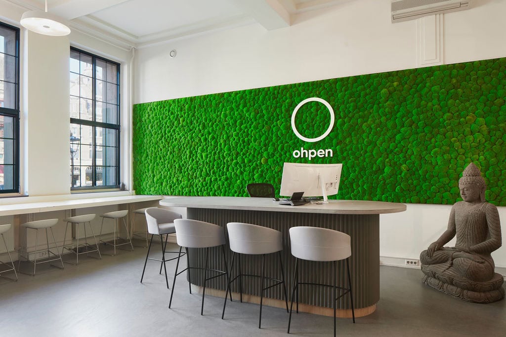 Reception area inside the Ohpen Amsterdam office designed by AIS. A vivid green moss wall behind reception houses the company logo.