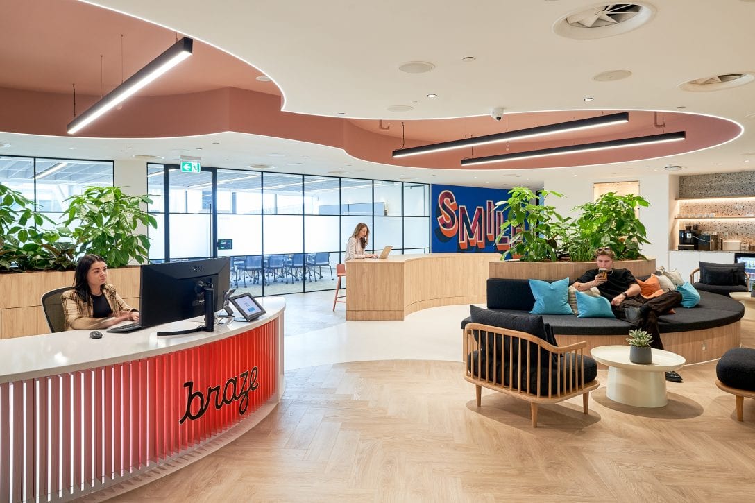Image shows people waiting in the Braze office reception area a design and build project by AIS where bright colours, finishes and furniture come together to create an experience design that embodies the Braze brand.