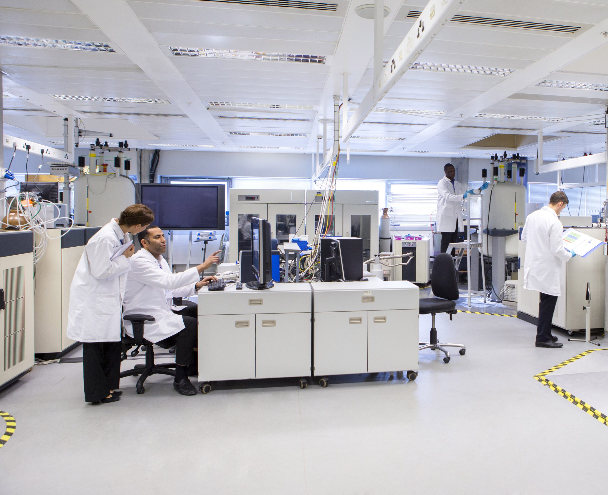 Scientists wearing white coats working in an open plan laboratory designed for optimal laboratory indoor air quality.