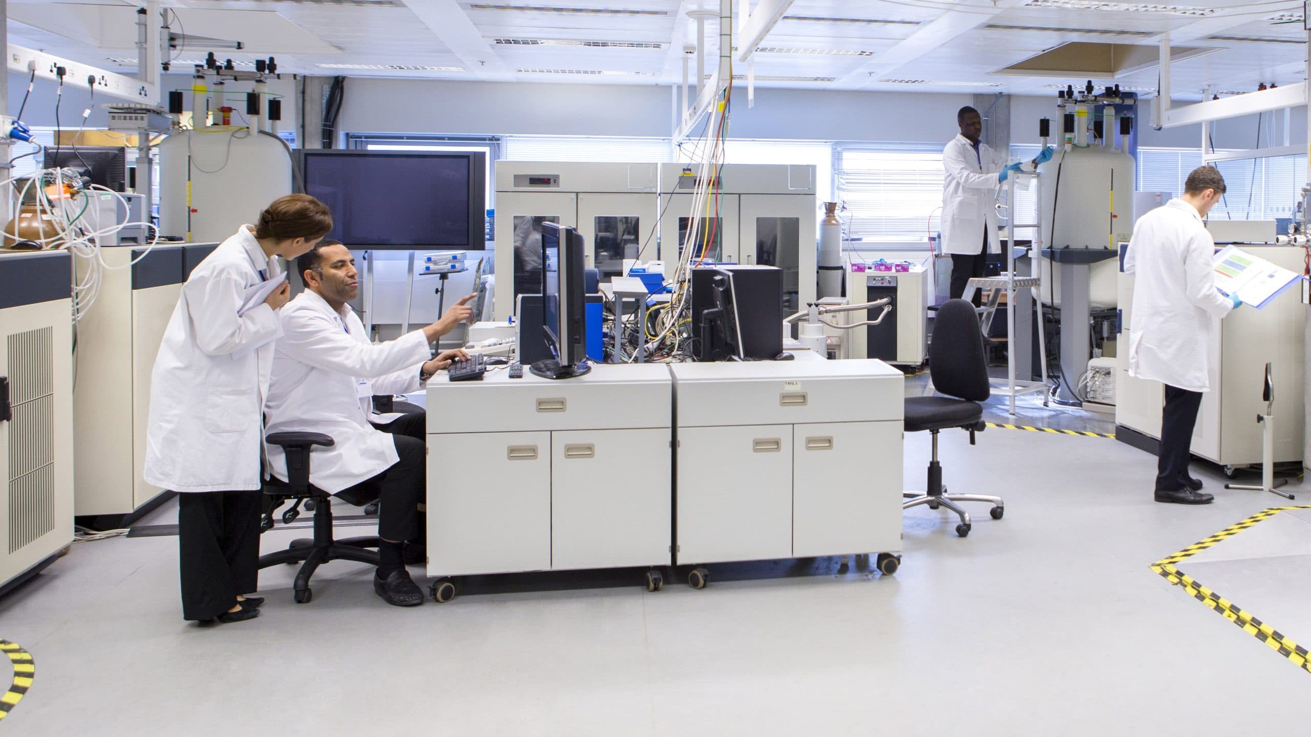 Scientists wearing white coats working in an open plan laboratory designed for optimal laboratory indoor air quality.