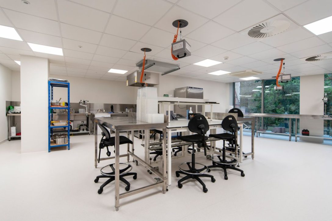 A high work bench with chairs surrounding it within the Hoxton Farms Lab space designed and built by AIS.
